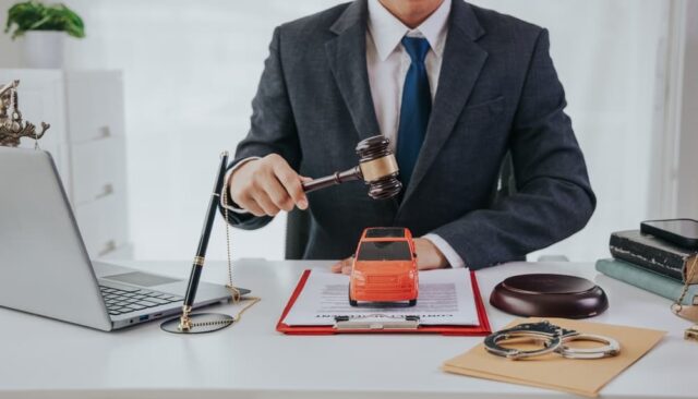 A judge's hand rests near a car model, legal documents, and a gavel, symbolizing a car accident case. 