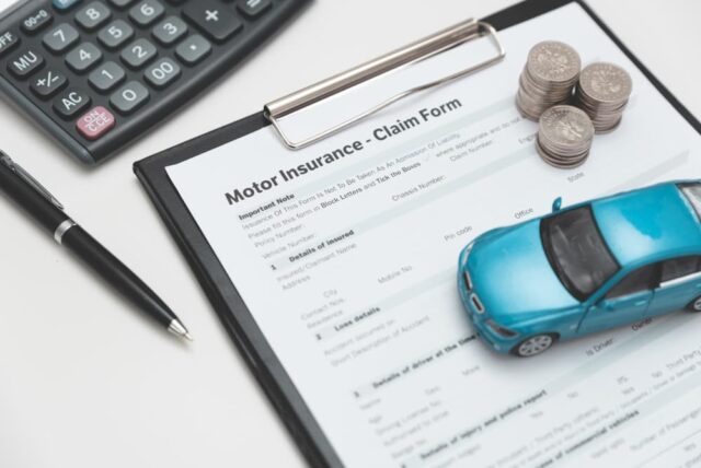 A car insurance claim form accompanied by a coin stack, a calculator, and a miniature car model. 