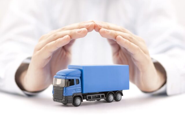 A miniature blue truck covered by hands symbolizing truck insurance.