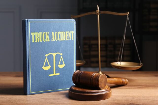 A truck accident law book, judge's gavel, and scales of justice placed on a wooden table.